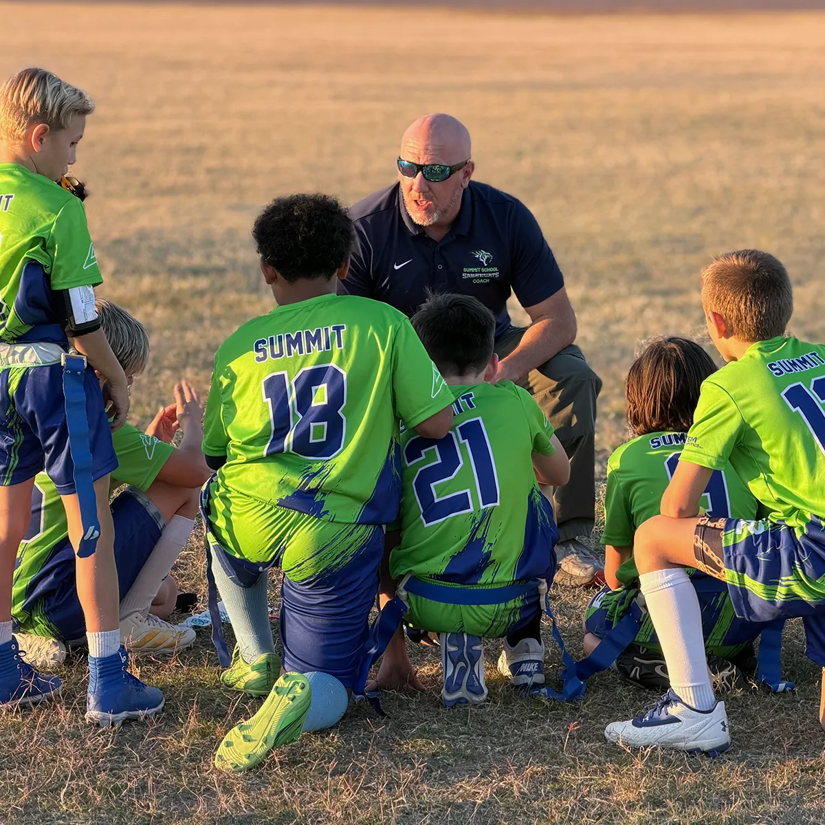 summit-elementary-athletics-team-coaching Summit School elementary athletes gathering with their coach during a team competition.