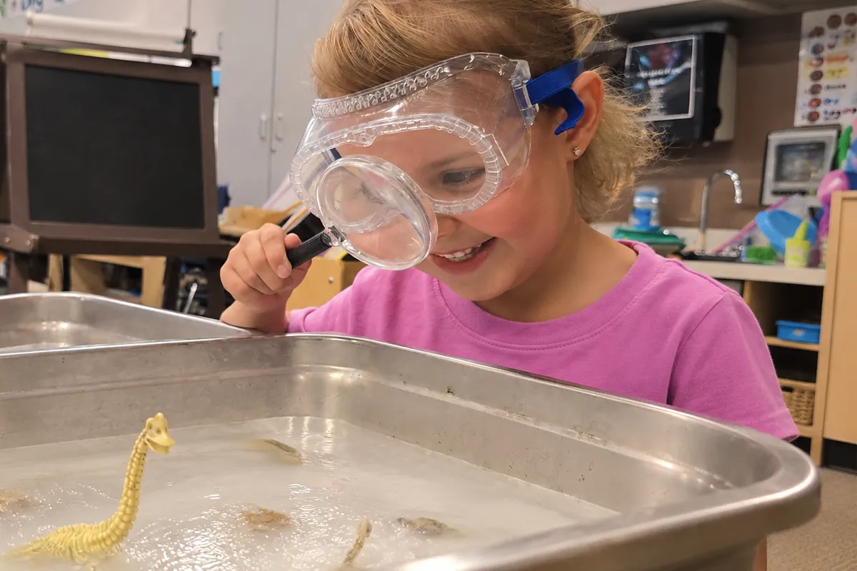 summit-preschool-science-discovery Summit preschool student using a magnifying glass during a hands-on science activity.