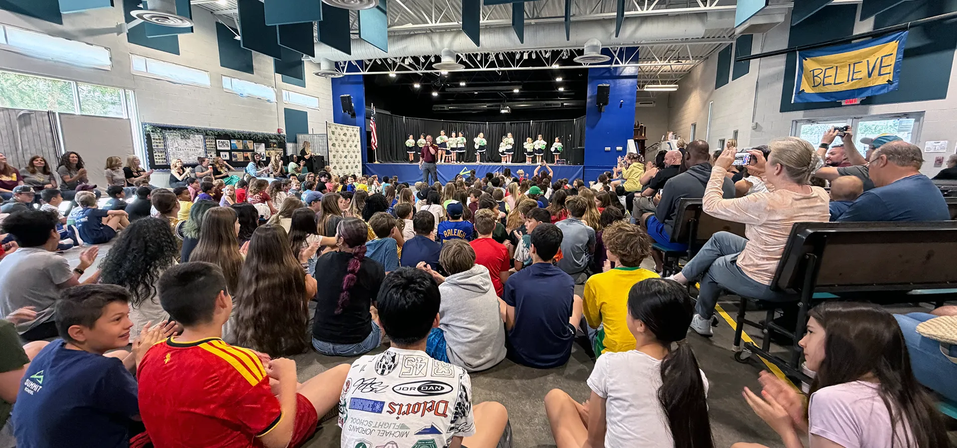 summit-school-morning-meeting-whole-school-community Summit School students and families gathered for Morning Meeting as students perform on stage.