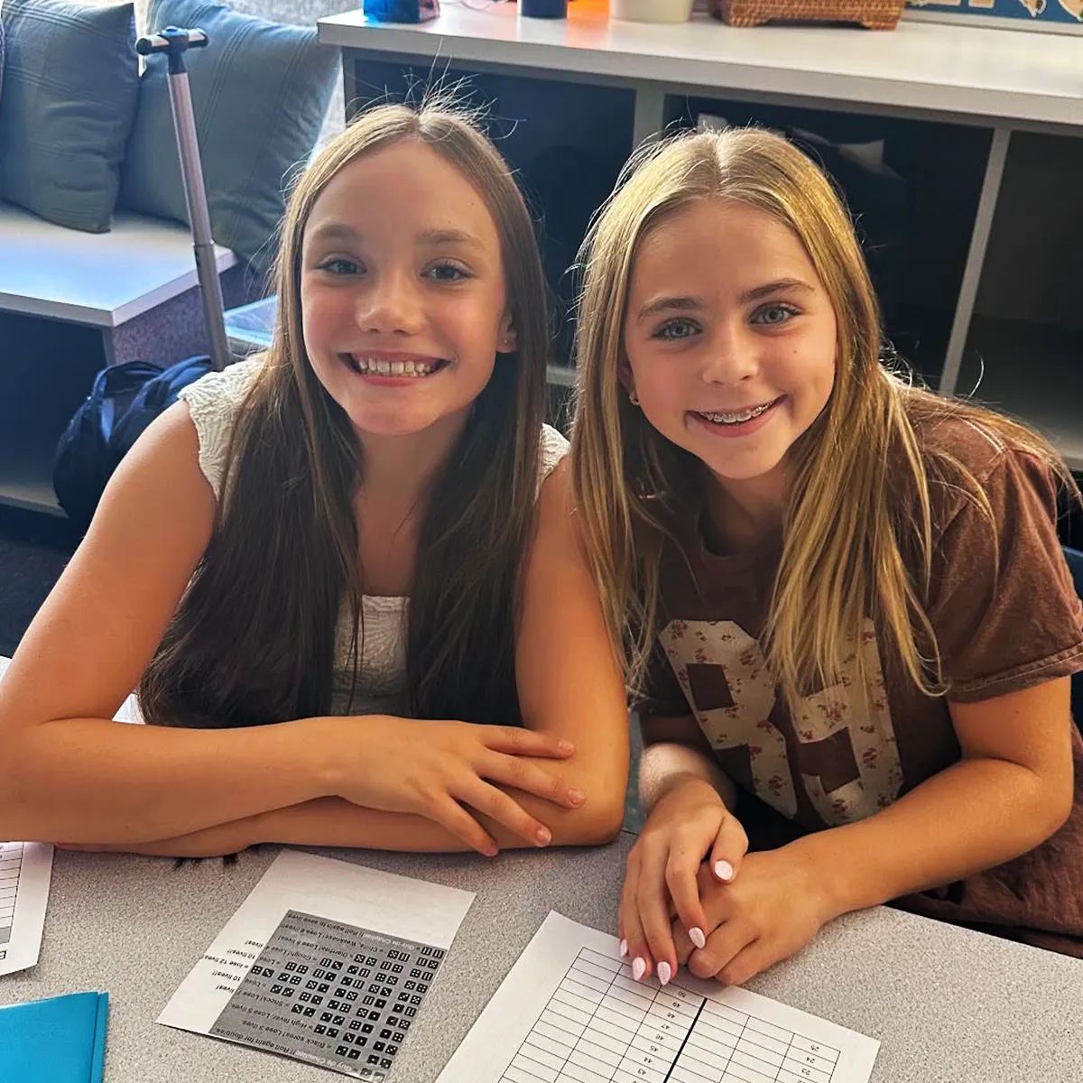 Two Summit School students smiling together in a classroom.